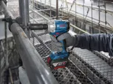 En person med sikkerhetsutstyr bruker en batteridrevet slagtrekker på et stillas.