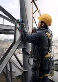 En person med sikkerhetsutstyr bruker en batteridrevet drill på en metallkonstruksjon.