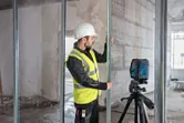 En person med sikkerhetsutstyr justerer en metallbolt med et lasernivelleringsverktøy.
