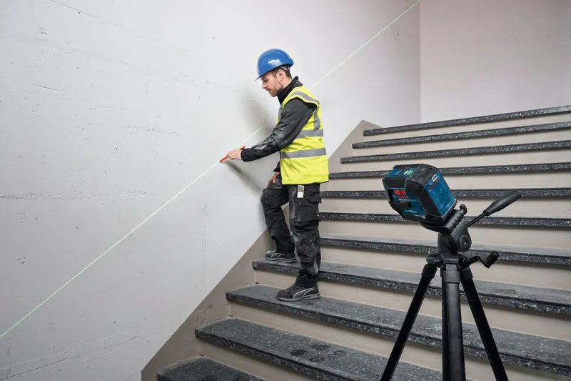 En person med sikkerhetsutstyr markerer en trappevegg med et lasernivelleringsverktøy.