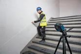 En person med sikkerhetsutstyr markerer en trappevegg med et lasernivelleringsverktøy.