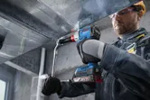 En person med sikkerhetsutstyr bruker en batteridrevet drill til å feste en metallkanal.