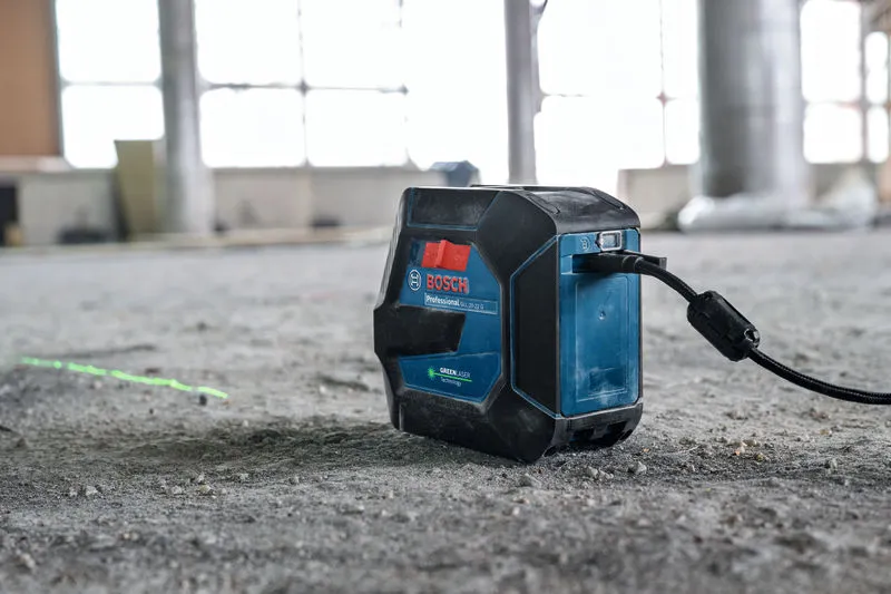 Lasernivelleringsverktøy projiserer en grønn linje på et betonggulv på en byggeplass.