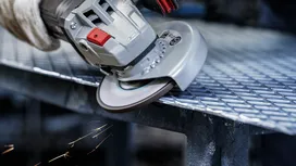 En person med sikkerhetsutstyr sliper en metallrist, noe som produserer gnister.