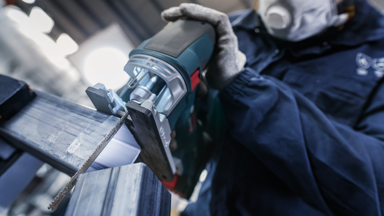 En person som bruker sikkerhetsutstyr bruker en bajonettsag til å kutte en metallbjelke.