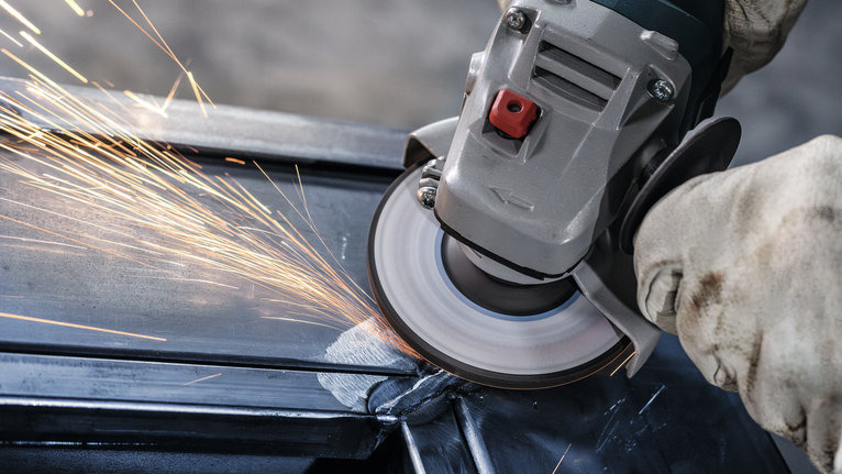 En person som bruker sikkerhetsutstyr sliper metall, noe som skaper sterke gnister.