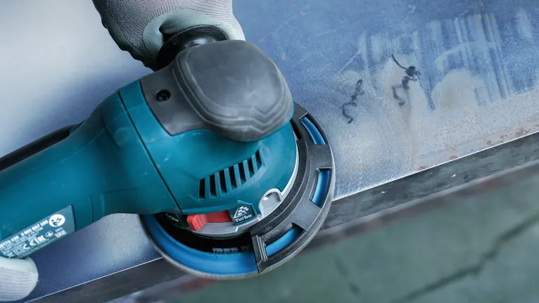 Person med sikkerhetsutstyr sliper en metalloverflate med et elektroverktøy.