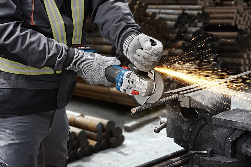 En person som bruker sikkerhetsutstyr bruker en vinkelsliper til å kutte en metallstang, noe som produserer gnister.