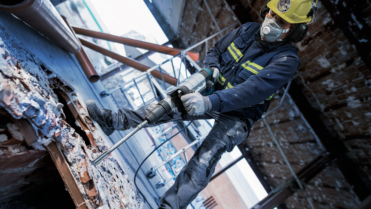 En person med sikkerhetsutstyr borer i betong på en byggeplass.
