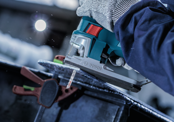 En person som bruker sikkerhetsutstyr bruker en stikksag til å skjære gjennom en metallplate.