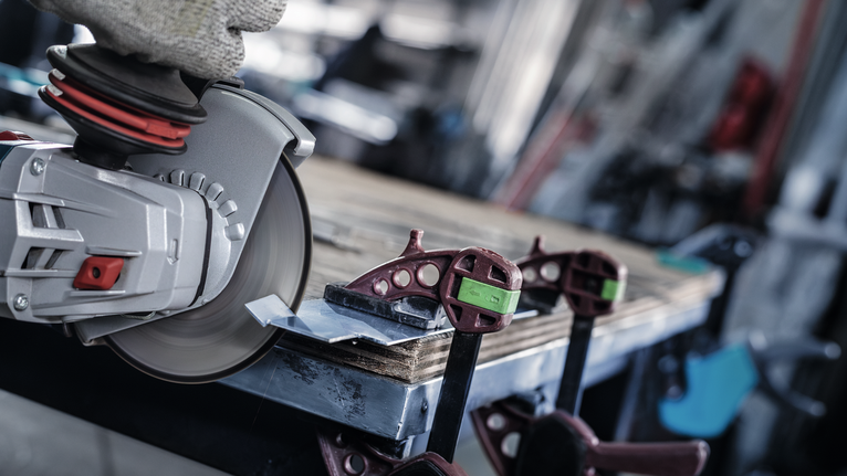 En person med sikkerhetsutstyr bruker en vinkelsliper til å skjære metall som er festet til en arbeidsbenk.