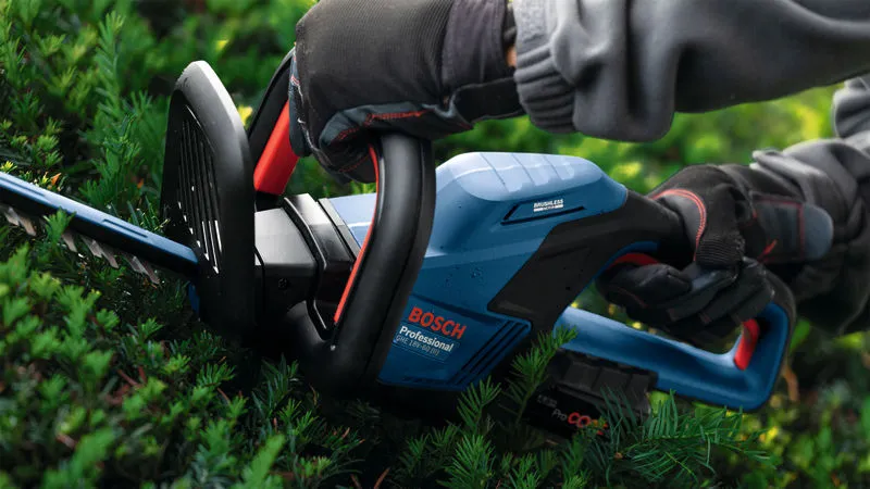 En person med sikkerhetsutstyr trimmer hekker med en batteridrevet hekksaks.
