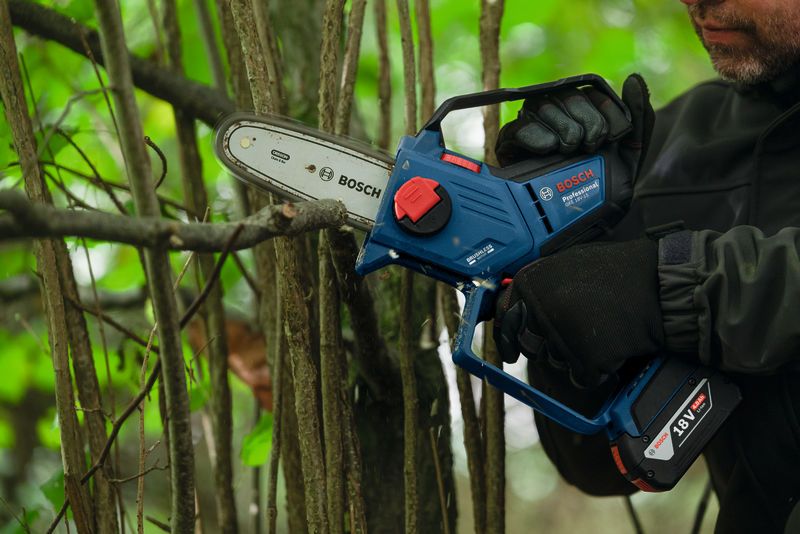 En person med sikkerhetsutstyr beskjærer tregrener med en batteridrevet beskjæringssag.