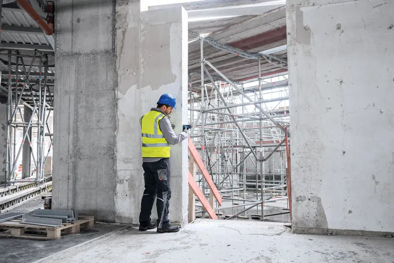 En person med sikkerhetsutstyr bruker en lasermåler på en byggeplass.