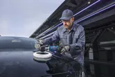 En person med sikkerhetsutstyr polerer en svart bil med en poleringsmaskin.