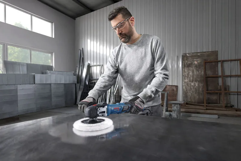 En person med sikkerhetsutstyr polerer en metalloverflate i et industriverksted.