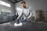 En person med sikkerhetsutstyr polerer en metalloverflate i et industriverksted.