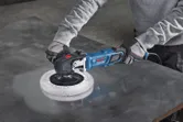 En person med sikkerhetsutstyr polerer en metallplate med en elektrisk poleringsmaskin.