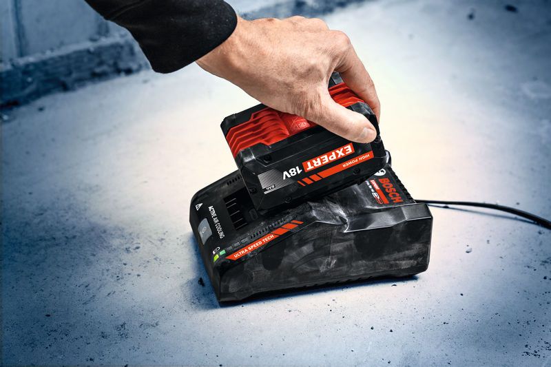 En person plasserer en rød og svart batteripakke på en ladestasjon.