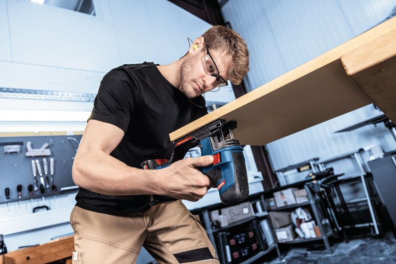 En person med sikkerhetsutstyr bruker en stikksag til å sagere tre i et verksted.