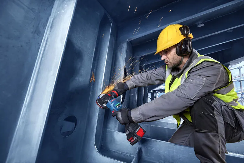 En person med sikkerhetsutstyr sliper metall med en batteridrevet vinkelsliper.