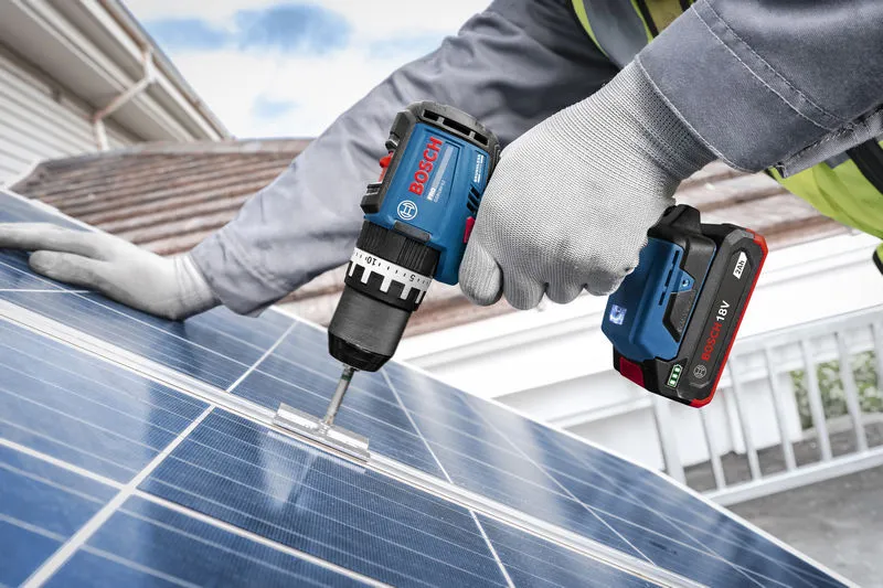 En person med sikkerhetsutstyr fester et feste til et solcellepanel ved hjelp av en batteridrevet slagbormaskin.