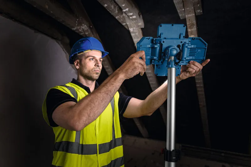 En arbeider med sikkerhetsutstyr justerer en trådløs arbeidsplasslampe på et stativ.