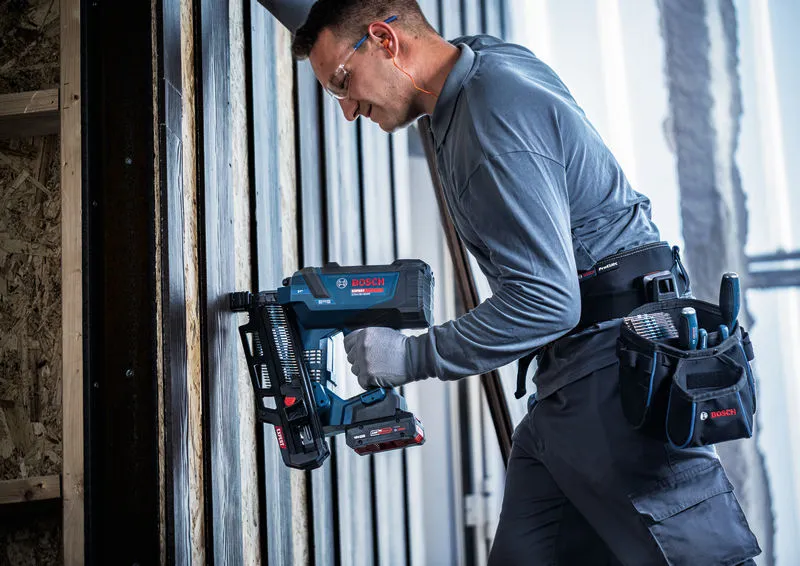 En person som bruker sikkerhetsutstyr bruker en batteridrevet trespikerpistol på en vertikal ramme.