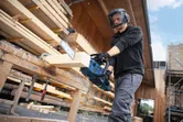 En person med sikkerhetsutstyr sager en trebjelke med en batteridrevet motorsag.