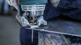 En person som bruker sikkerhetsutstyr bruker en stikksag til å kutte en metallplate.