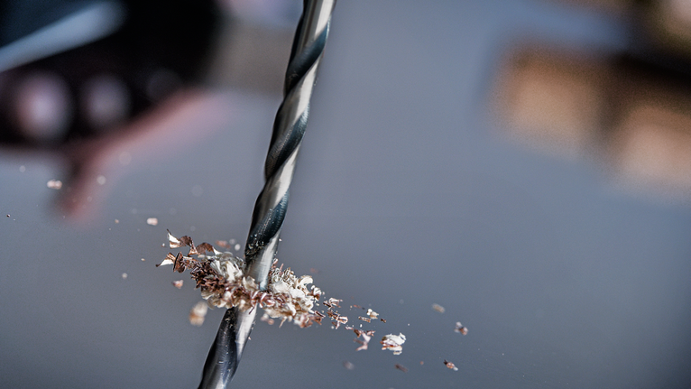 Borekrone som lager et hull i en metallplate med spredt metallspon.