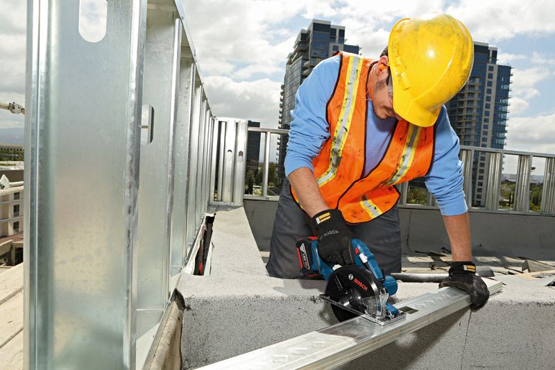 A person wearing safety equipment cuts a metal beam with a cordless circular saw.