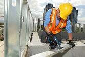A person wearing safety equipment cuts a metal beam with a cordless circular saw.