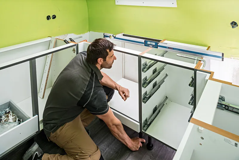 A person installs cabinetry while using a digital inclinometer on the counter.