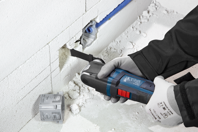 Person wearing safety equipment cuts a slot into a wall with a power tool.