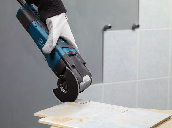 Person wearing safety equipment cuts a ceramic tile with a handheld power cutter.