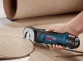 Person cutting a circular shape from cork sheet using a cordless universal shear.