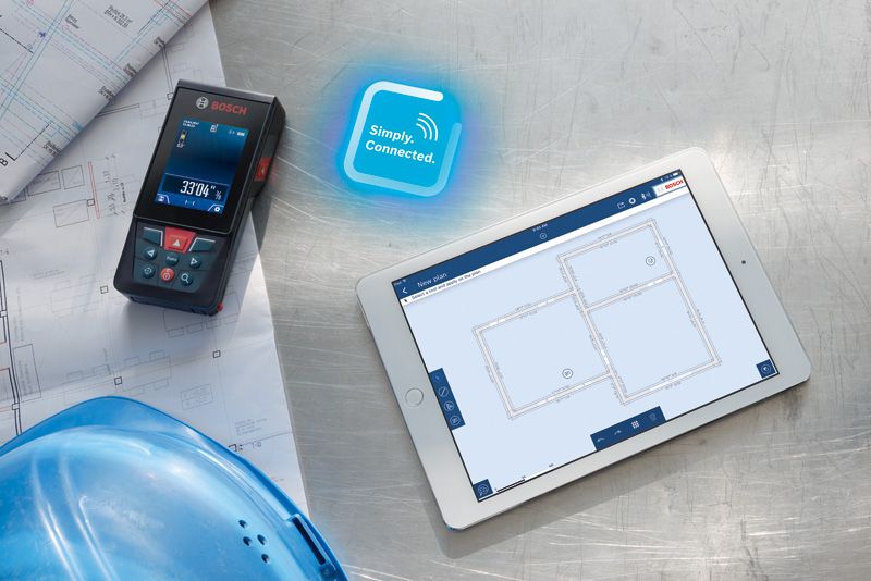 Laser measure on blueprints beside a digital tablet displaying building plans.