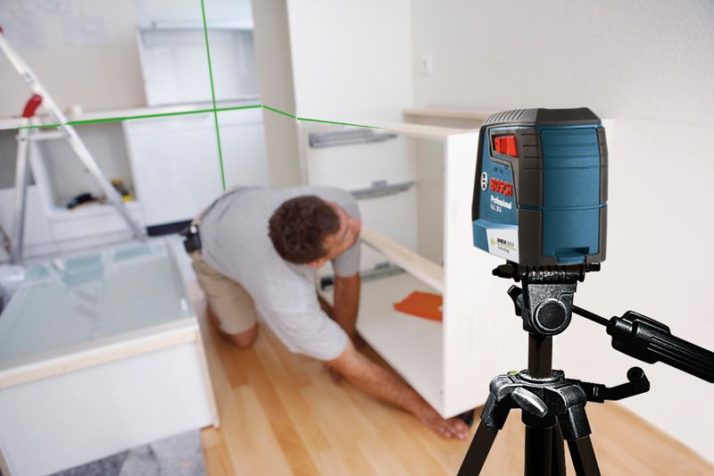A person installs a cabinet in a kitchen using a laser leveling tool on a tripod.