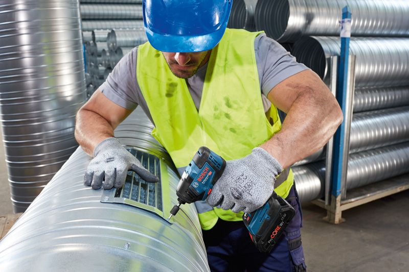 A person wearing safety equipment fastens a vent cover to a metal duct with a power tool.