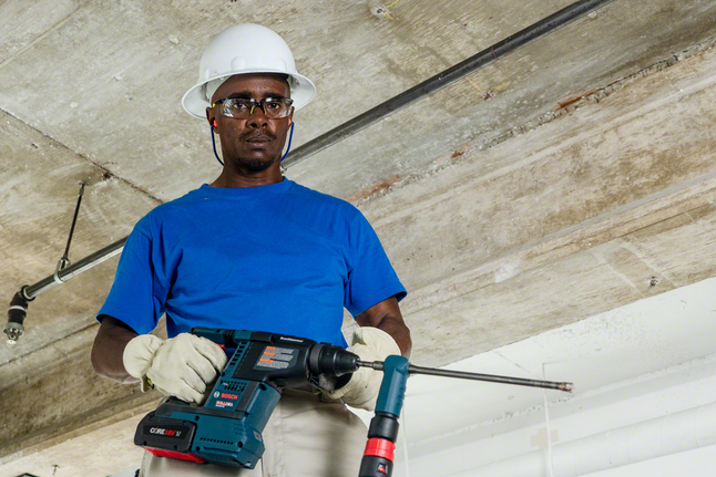 Person wearing safety equipment drills into a concrete ceiling with a rotary hammer.