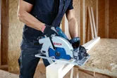 A person wearing safety equipment uses a circular saw to cut a wooden board.