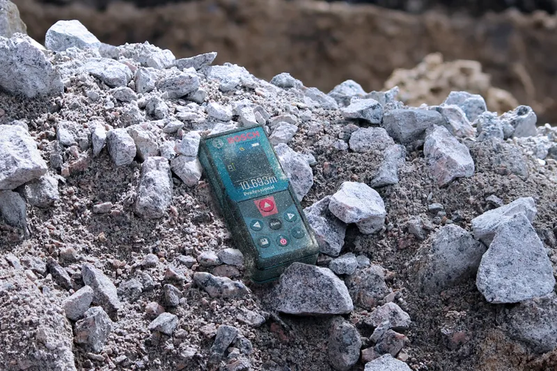 A laser measure resting on a pile of rocks at a construction site.