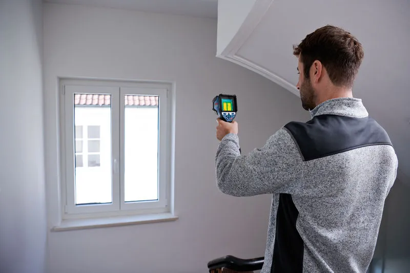 A person uses a thermo camera to inspect a window indoors.