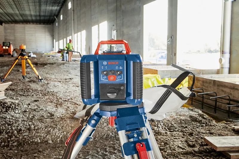 Laser leveling tool set on a tripod at a construction site, person wearing safety equipment in background.