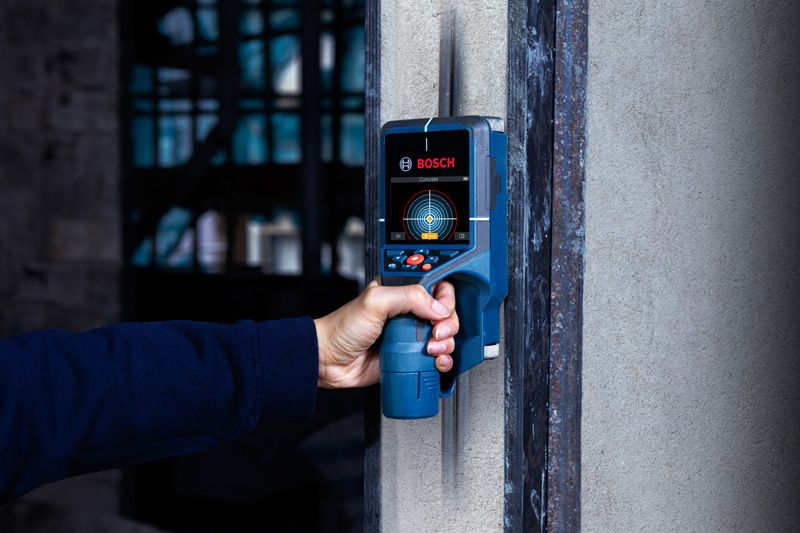 Person scanning a wall using a detector for hidden objects.