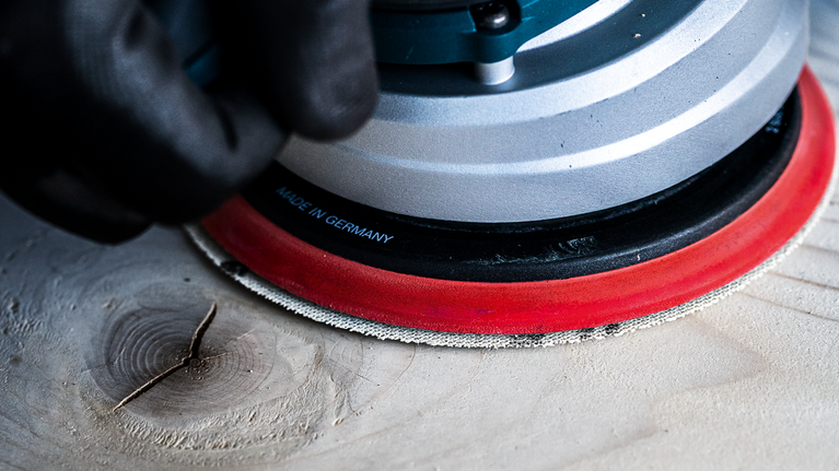 EXPERT M480 Starter Kit for Random Orbital Sanders 125 mm 7-pc Person wearing safety equipment sanding a wooden surface with a power tool.