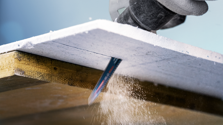 Person wearing safety equipment uses a saw to cut lines in a sheet of material.