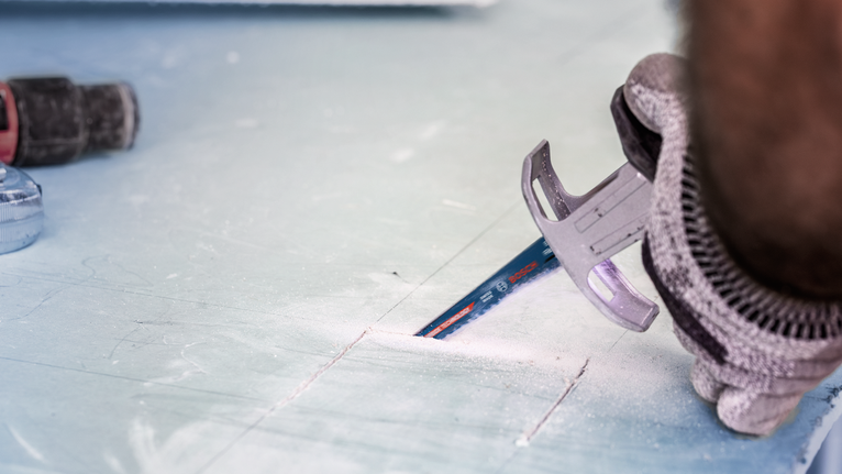 Person wearing safety equipment cuts drywall with a power tool.