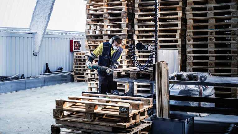 Person wearing safety equipment uses a reciprocating saw to cut through a wooden crate.